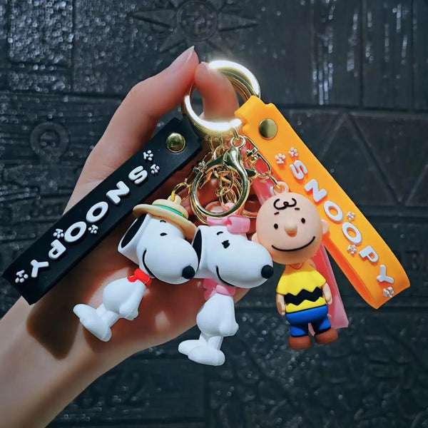 A hand holds a keychain set featuring Snoopy characters in various styles, including a dog and a character resembling Charlie