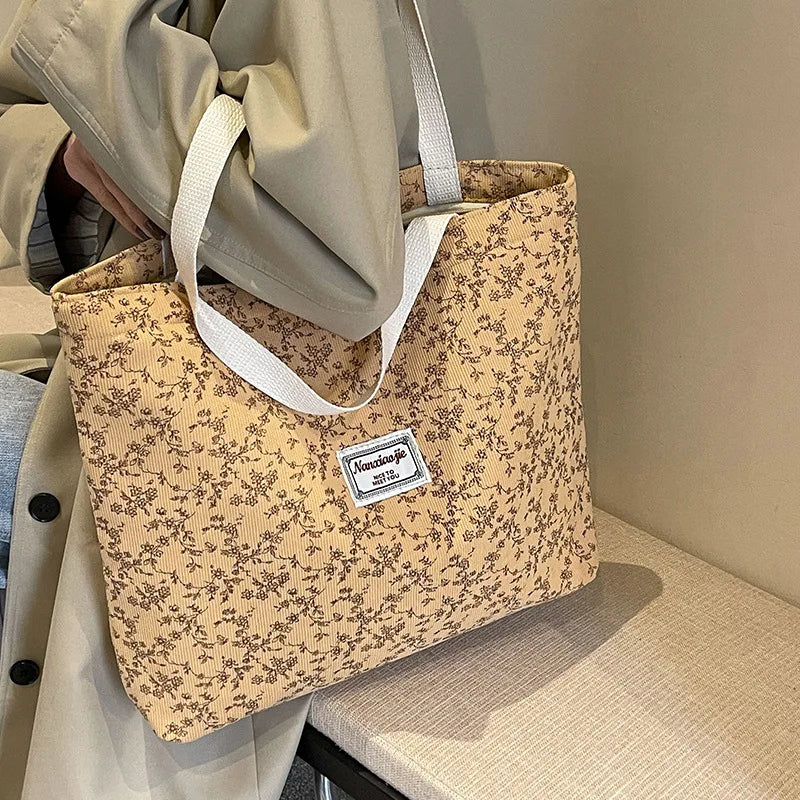 A beige bohemian corduroy tote bag with a floral pattern is held by a person.