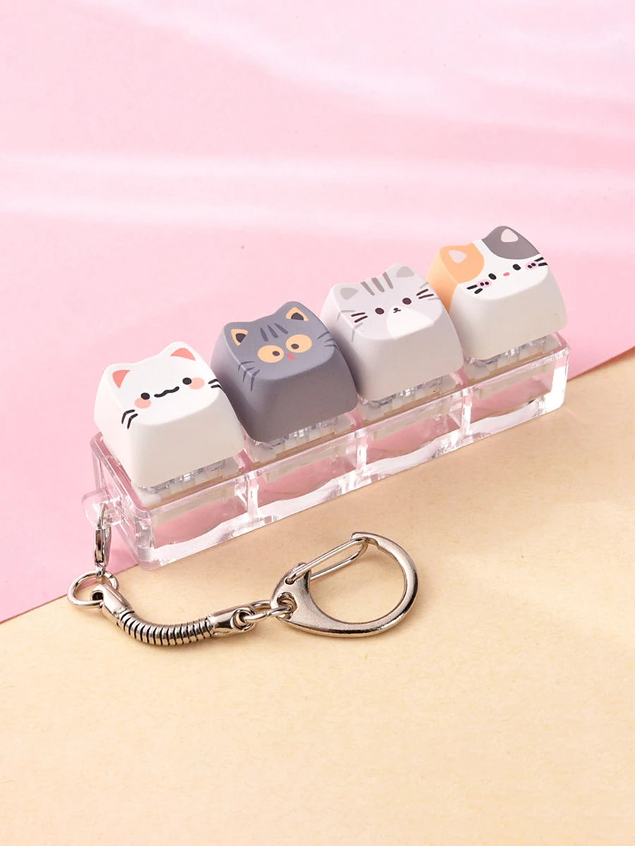 A row of pastel-colored kawaii cat keycaps arranged in a clear plastic holder with a silver bag charm.