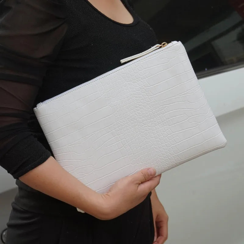A woman holds a white leather clutch bag with a gold zipper and alligator print texture.