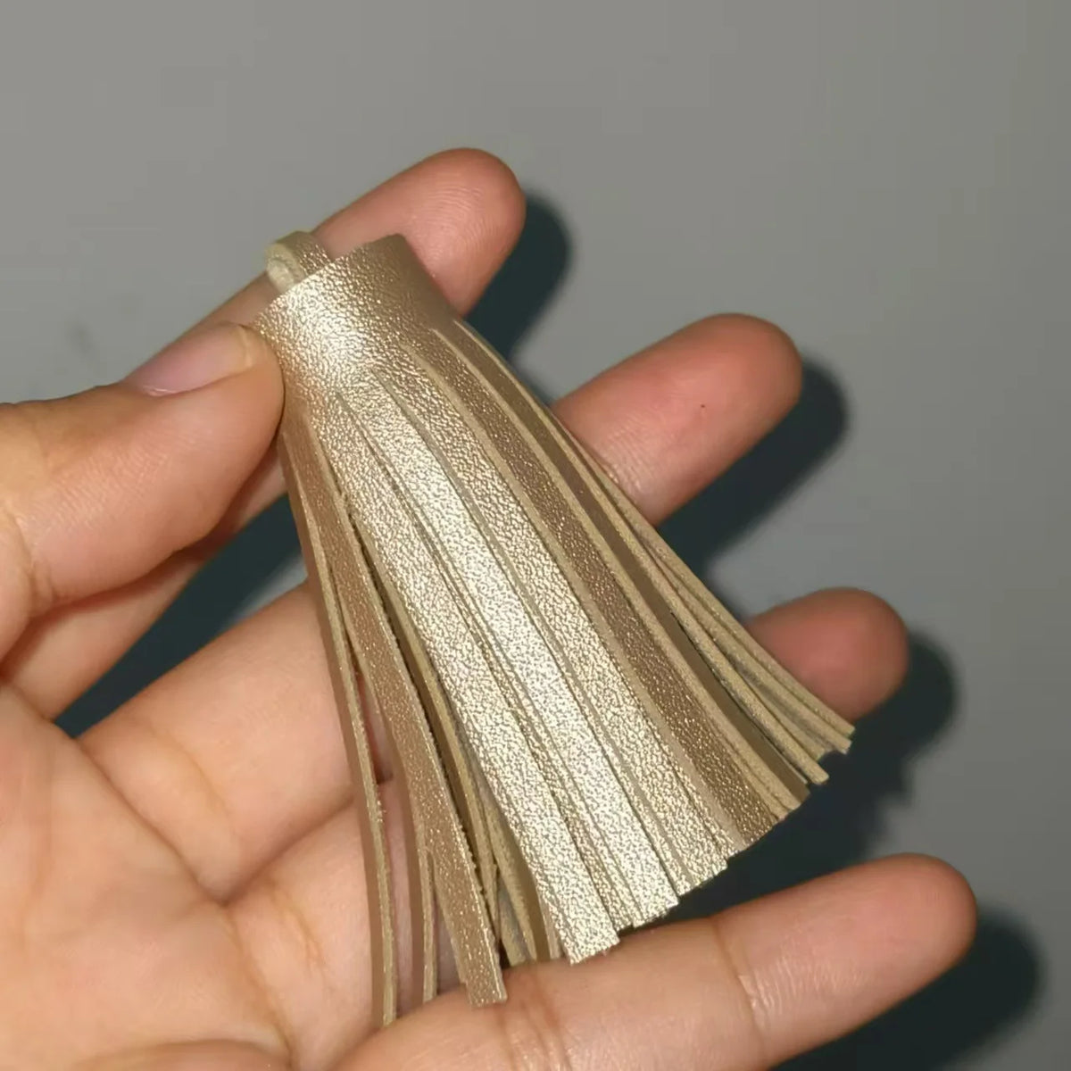 A hand holds a set of gold leather tassel fringe craft supplies.