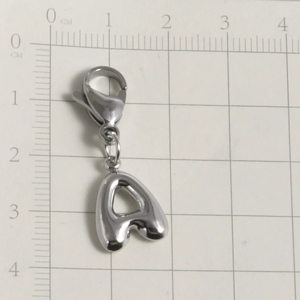 Silver stainless steel alphabet letter charm with a lobster clasp shown against a ruler.