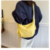 A yellow canvas crossbody bag is shown hanging from a navy blue sweatshirt, next to a white paneled wall.