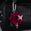A deep magenta rose flower and a silver butterfly charm attached to a black leather handbag.