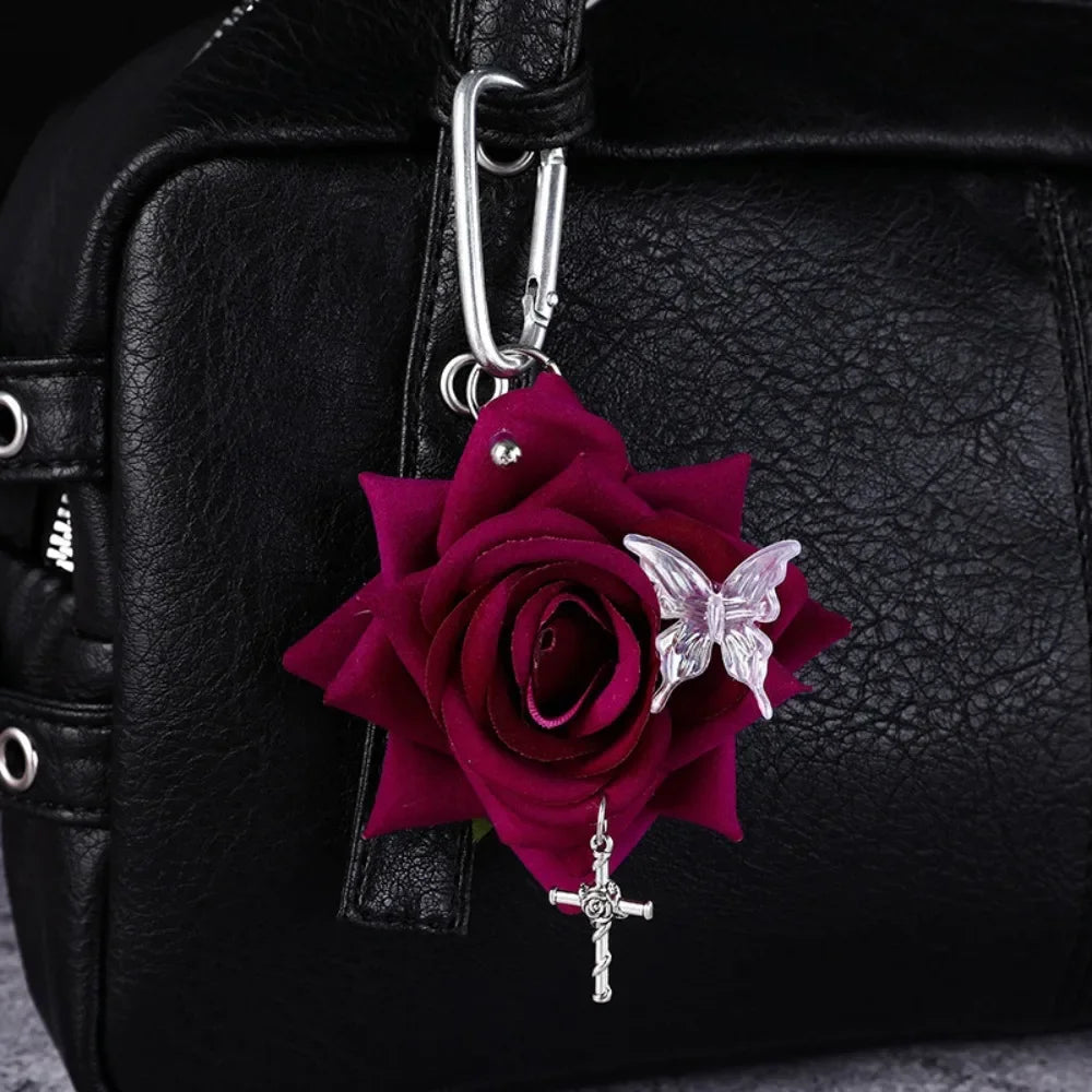 A deep magenta rose flower and a silver butterfly charm attached to a black leather handbag.