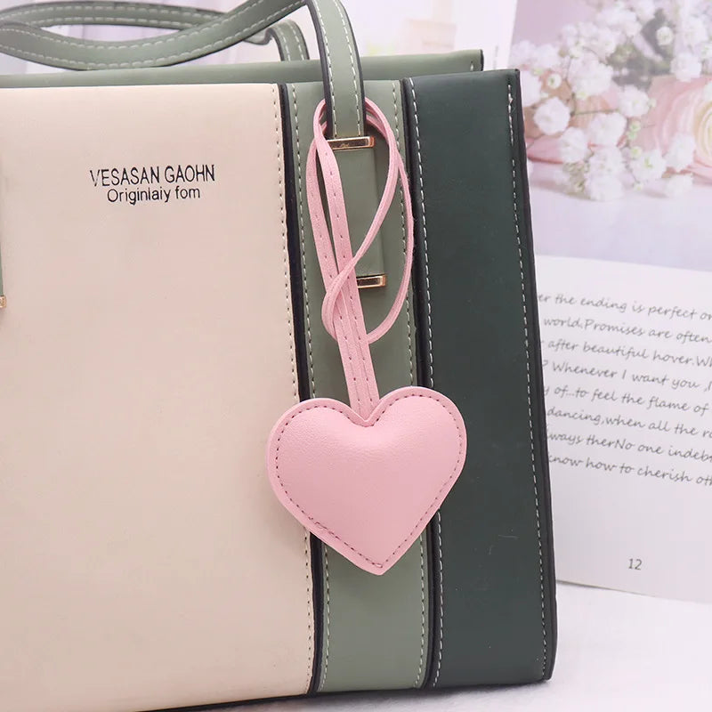 A light beige leather pouch with a pink heart charm and green stripes, featuring the VESASAN GAOHN brand.
