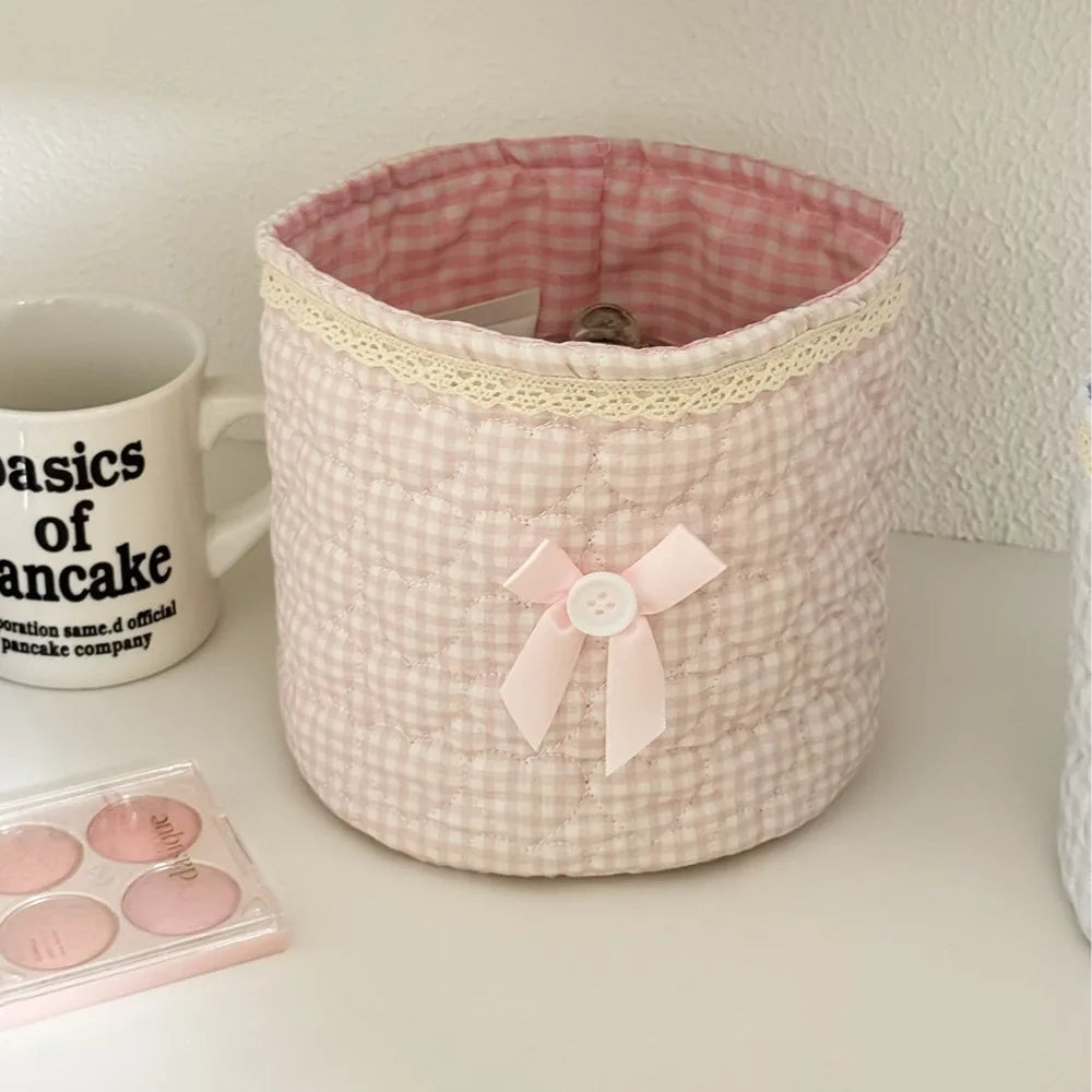 Cesta de almacenamiento de corazón acolchado rosa de algodón con ribete de encaje, junto a una taza y artículos rosas.