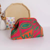 A vibrant knitted clip bag with an orange and pink pattern rests in front of a beige cardstock shape.