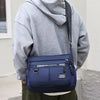 A person is holding a navy blue men's business crossbody bag with a gray hoodie.