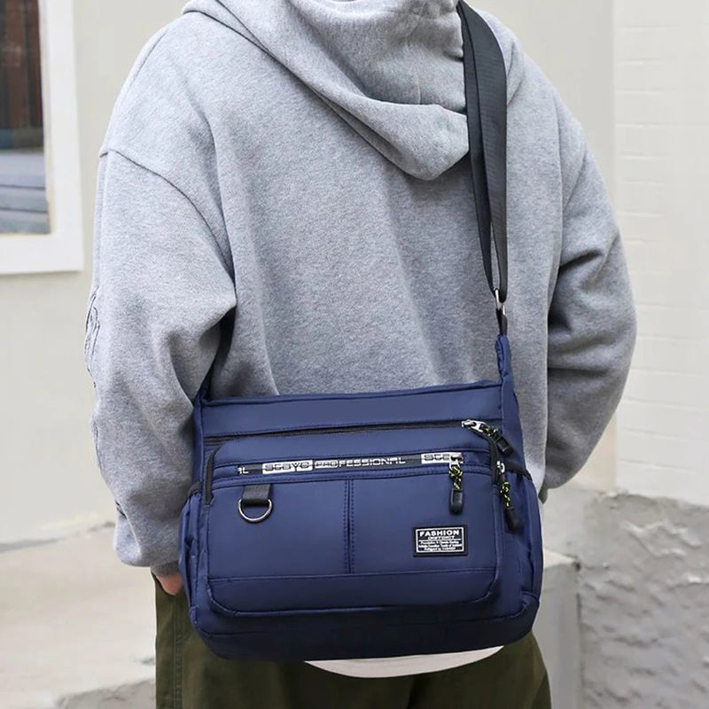 A person is holding a navy blue men's business crossbody bag with a gray hoodie.