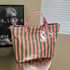 A pink and green striped transparent waterproof PVC tote bag resting on a wooden surface.