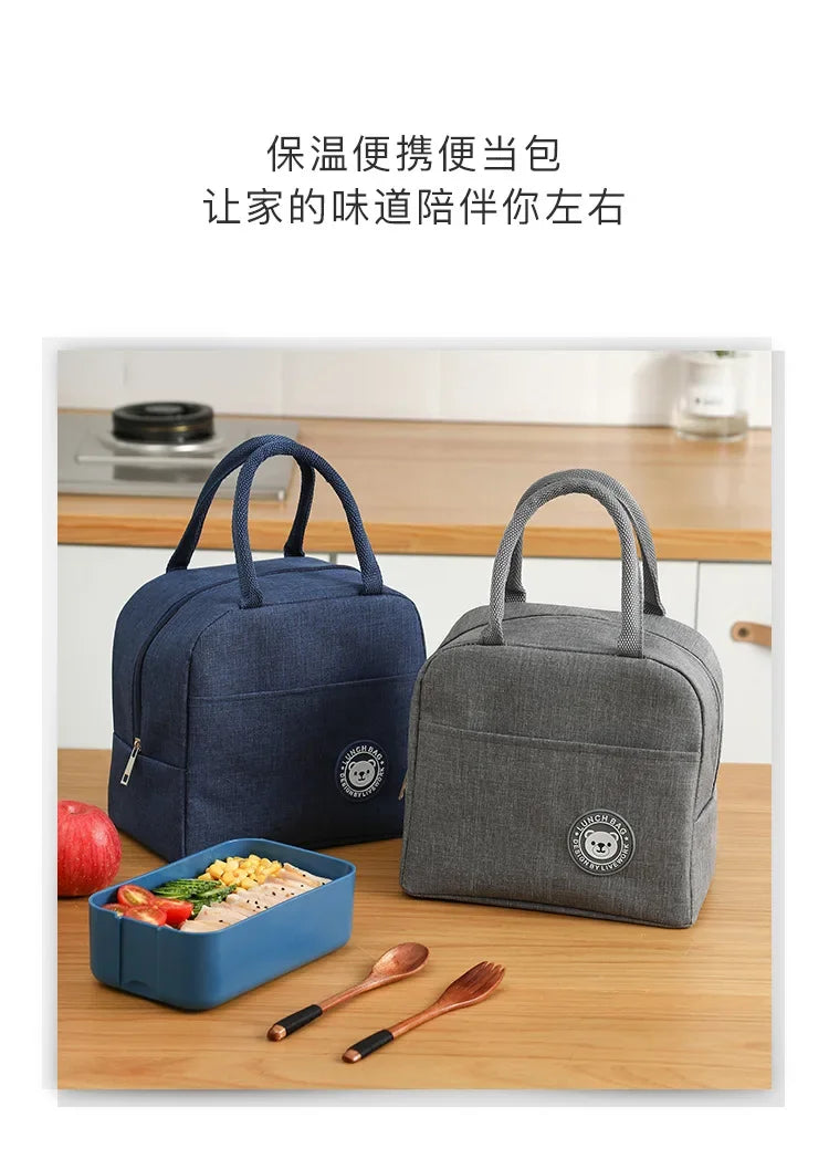 Two reusable insulated lunch bags, one navy blue and one gray, are shown next to a wooden cutting board with food and utensil