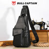 A black genuine leather sling backpack with a leather strap and pocket displayed on a wooden surface.