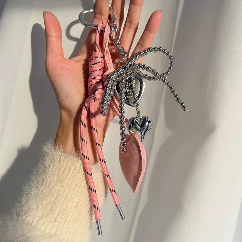 A hand holds a collection of pink and silver beaded keychains and charms.