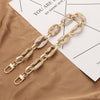 A gold-toned acrylic handbag strap chain with marbled white and beige beads resting on a brown fabric next to a piece of pape