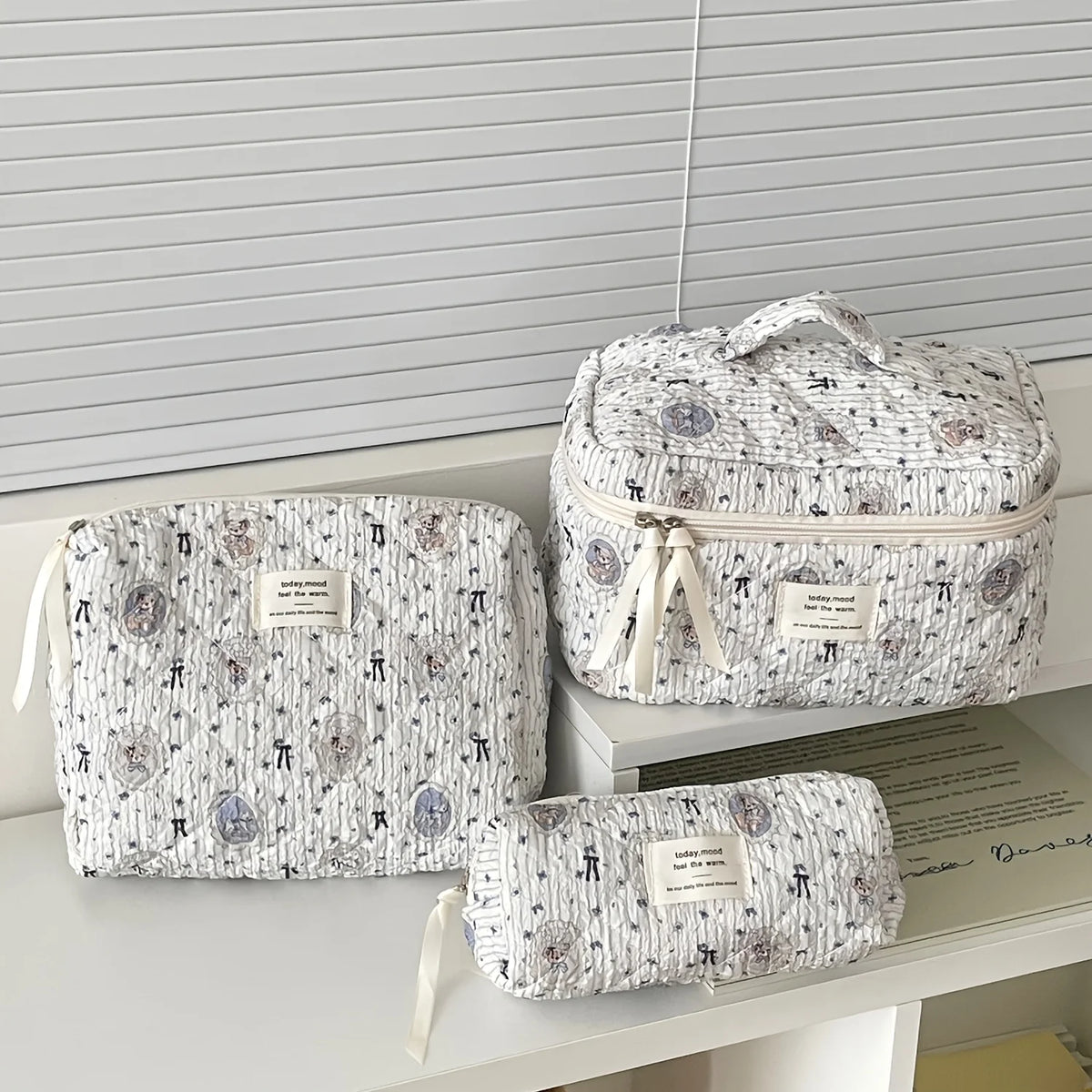 A set of quilted cotton makeup organizers in white and gray patterned fabric resting on a white shelf.