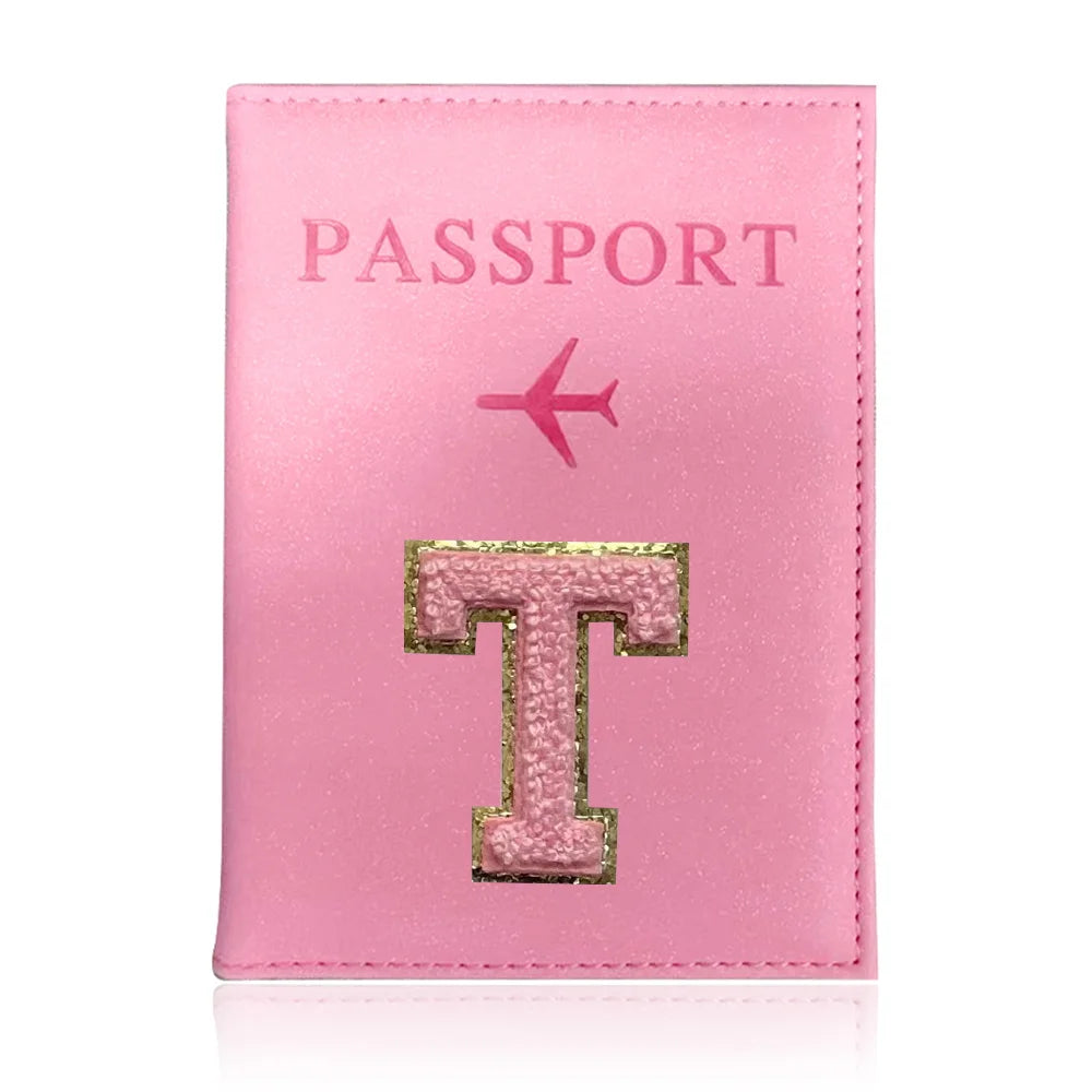 A pink leather passport holder with a gold initial T and a pink airplane emblem.
