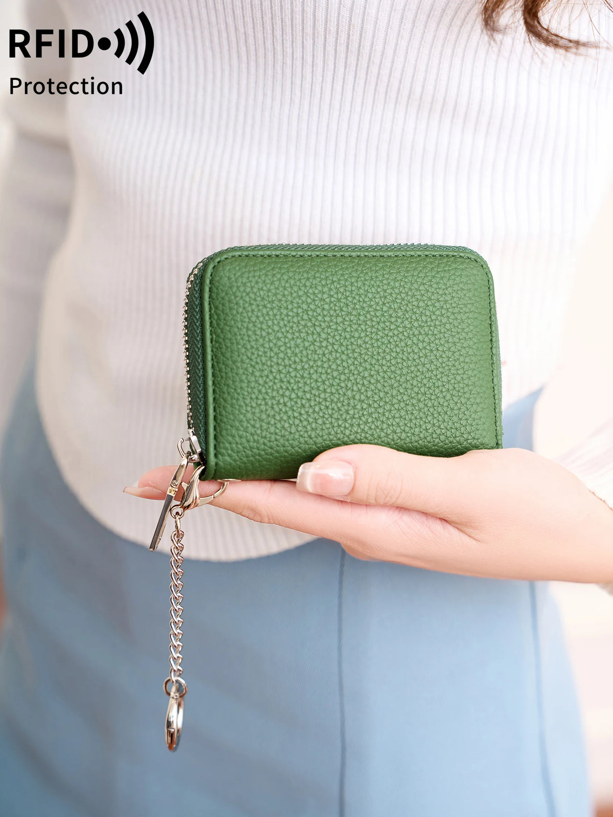 A hand holds a green accordion-style wallet with a zipper and chain attached, against a light background.