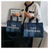 A woman holds a dark blue tote bag against a white sweater.