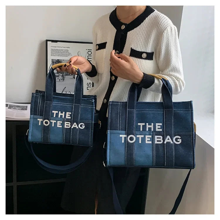 A woman holds a dark blue tote bag against a white sweater.