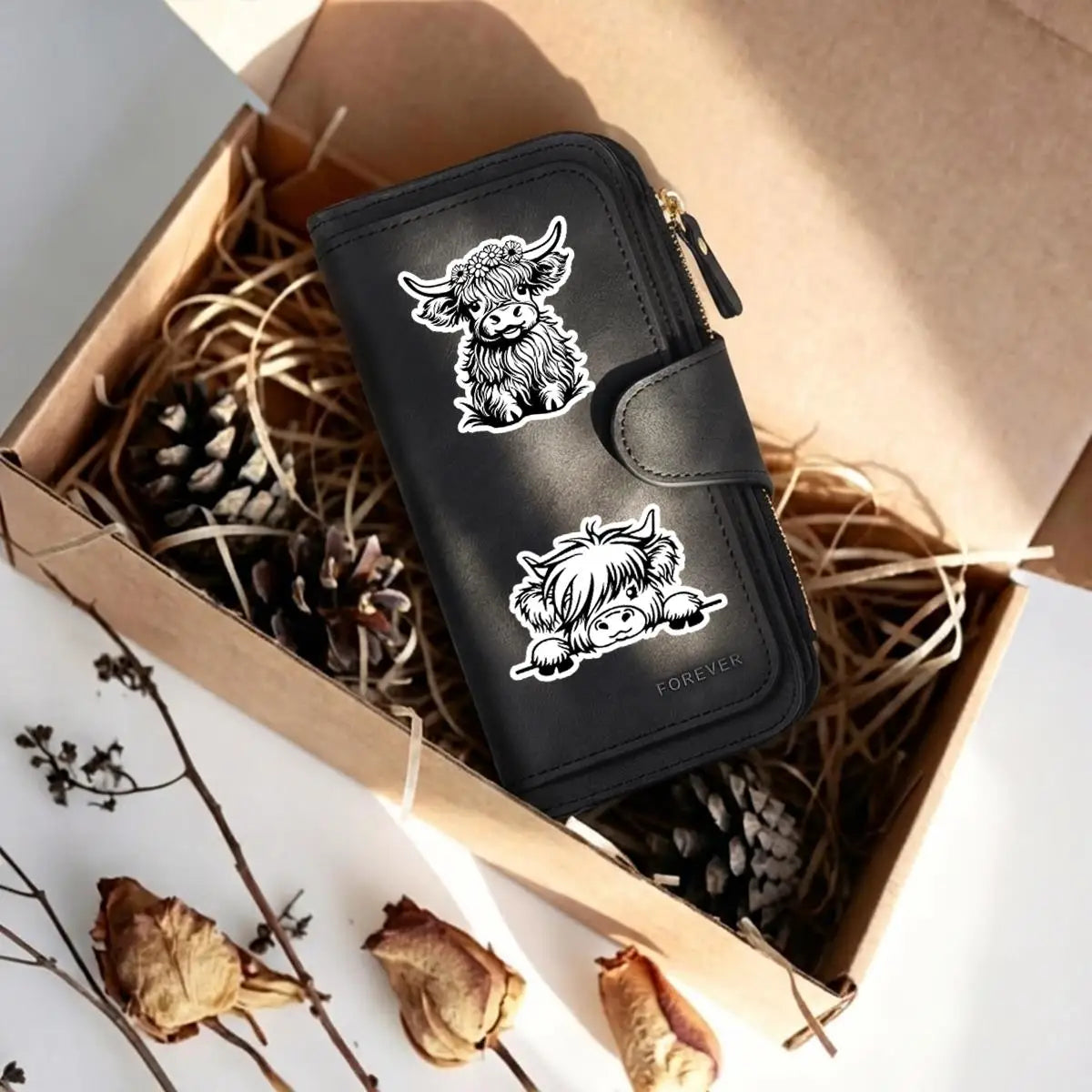 Cartera de cuero sintético negro con diseño de vaca, apoyada en una caja de cartón