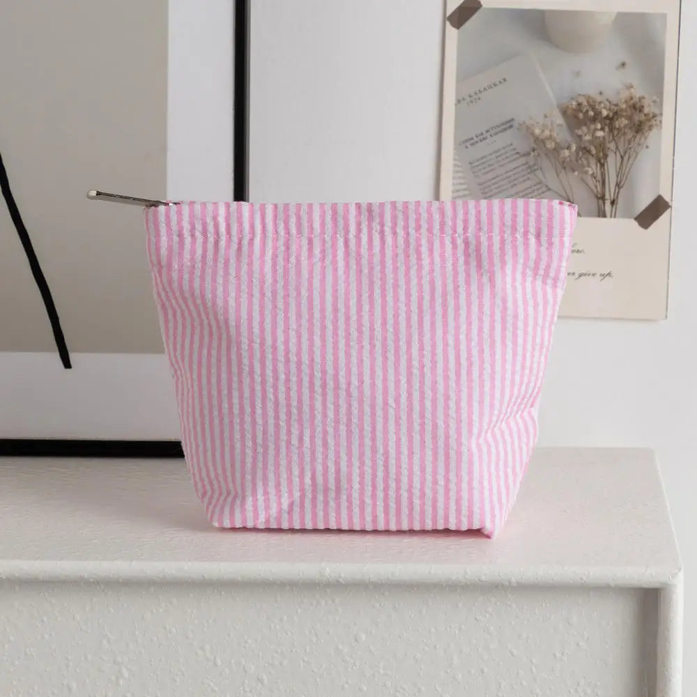 Bolso de crochet rayado rosa y blanco sobre una estantería blanca junto a un cuadro enmarcado.