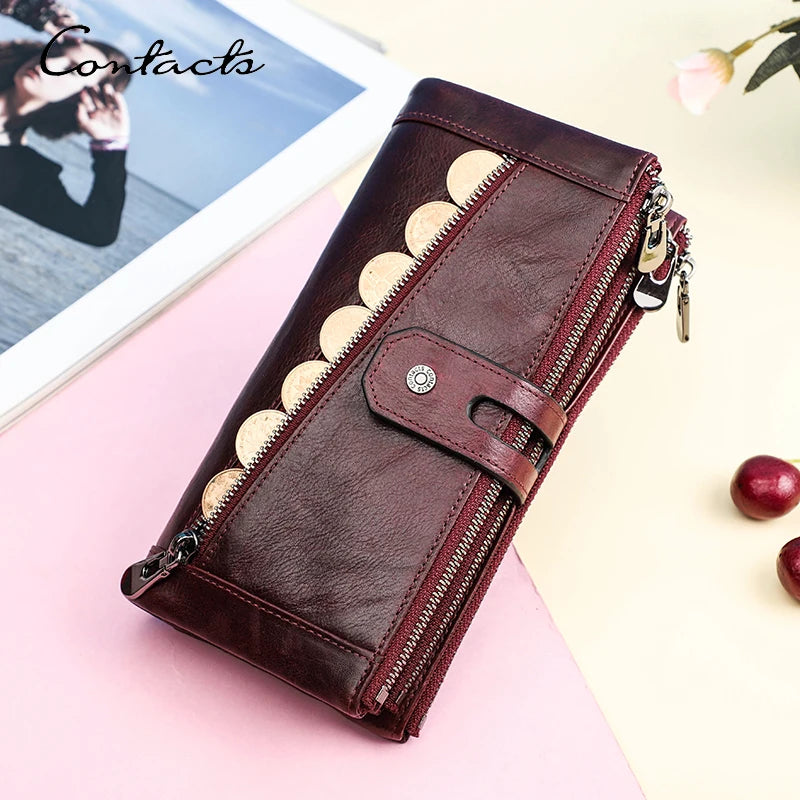 A dark brown genuine leather vintage clutch wallet with gold stitching and a silver zipper is displayed on a pink surface.