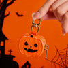 An orange carved pumpkin keychain accessory being held against a dark background with bats and spiderwebs.