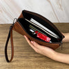 Une main tient un porte-monnaie clutch en cuir marron à fermeture éclair ouverte, montrant une carte argentée et un objet rou