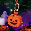 An orange pumpkin-shaped mini PU leather keychain accessory hanging from a green pine branch.