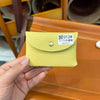 A hand holds a light yellow quilted leather card holder with a silver stud and a white tag displaying the number 012#
