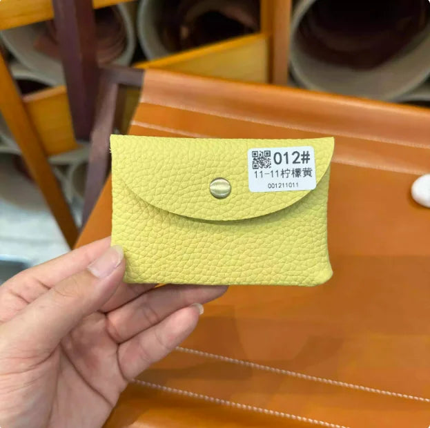 A hand holds a light yellow quilted leather card holder with a silver stud and a white tag displaying the number 012#