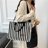 Une femme tient un sac bandoulière à motif rayé noir et blanc sur un fond blanc.