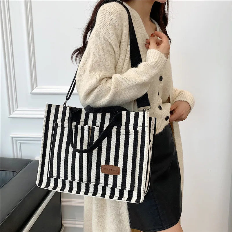 Une femme tient un sac bandoulière à motif rayé noir et blanc sur un fond blanc.