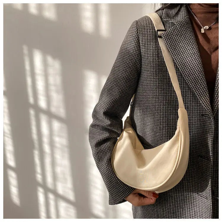 A woman wearing a gray plaid blazer holds a beige sling crossbody bag.