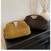 A close-up of a straw woven tote handbag in yellow and dark brown colors resting on a dark cabinet.