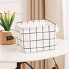 A white and black checkered storage basket is placed on a white table next to a potted succulent plant.