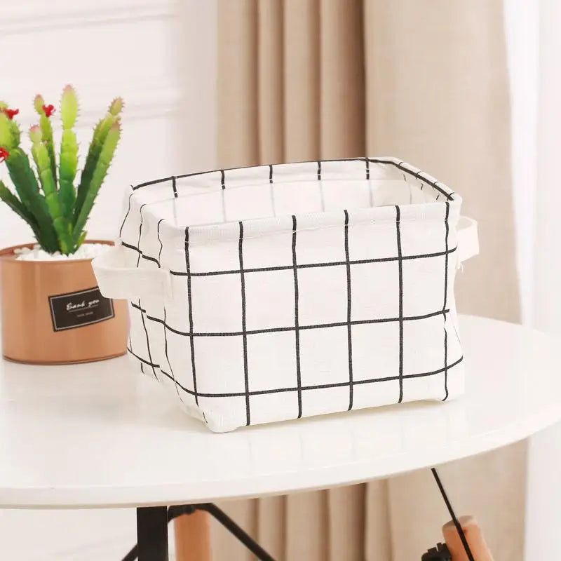 A white and black checkered storage basket is placed on a white table next to a potted succulent plant.
