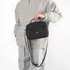 A man wearing a gray jacket is holding a black compact waterproof crossbody messenger bag.