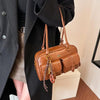 A brown leather vintage letter print crossbody bag is shown hanging from a black coat sleeve.