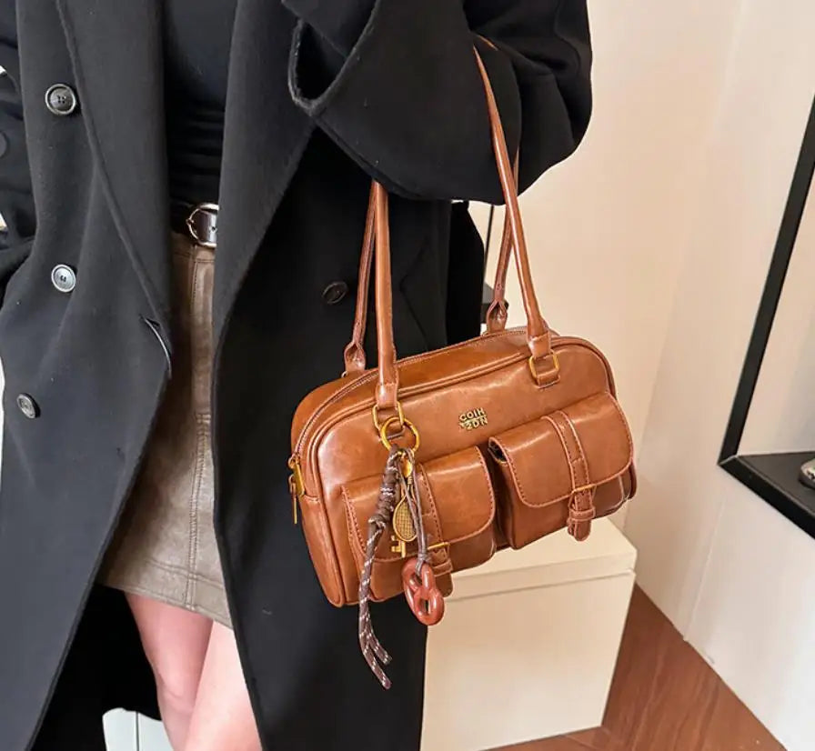 A brown leather vintage letter print crossbody bag is shown hanging from a black coat sleeve.