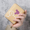 A hand holds a light beige mini zipper coin purse featuring a white cartoon elephant design and a purple glitter detail.