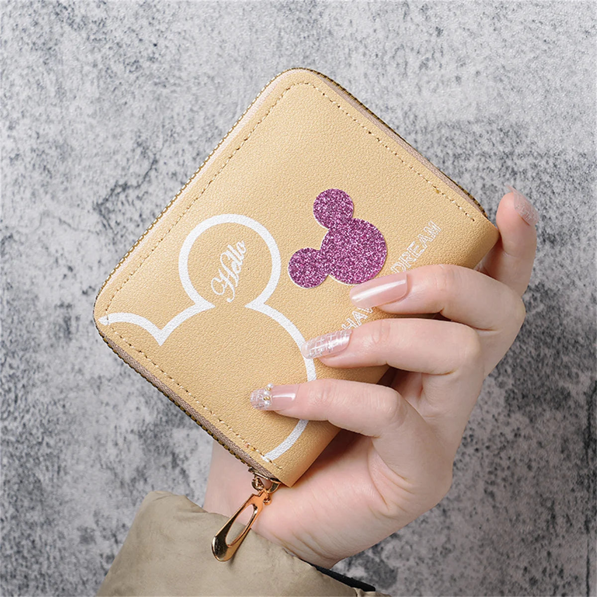 A hand holds a light beige mini zipper coin purse featuring a white cartoon elephant design and a purple glitter detail.