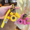 A hand holds a yellow fitness dumbbell keychain charm with black and pink components.