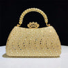 A gold crystal-embellished evening clutch bag with a chain strap resting on a white surface.