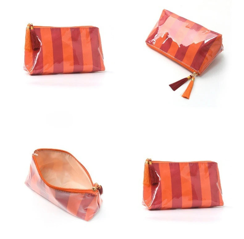 A square, glossy orange and brown striped cosmetic travel pouch with a dangling fringe.