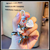 A hand holds a shiny metallic balloon dog keychain charm with a loop and a heart tag.