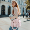 A young woman wearing a pink quilted insulated lunch bag and light top stands outdoors in front of a modern building.