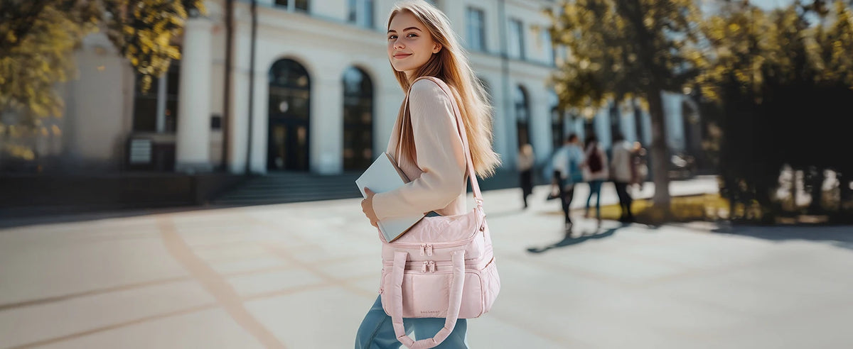 A young woman wearing a pink quilted insulated lunch bag and light top stands outdoors in front of a modern building.