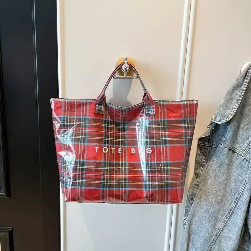 A red and blue plaid transparent waterproof PVC tote bag hanging on a white door.